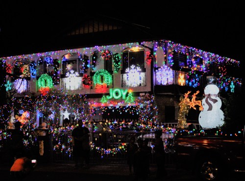 A house decorated with colorful Christmas lights, featuring snowflakes, wreaths, and a large snowman.