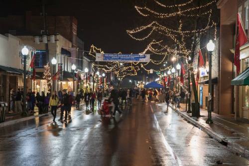 A festive street at night, adorned with lights and flags, bustling with people celebrating an event.