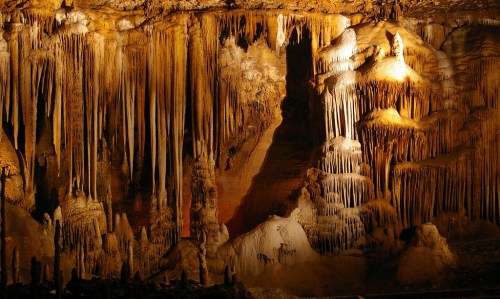 Stalactites and stalagmites in a dimly lit cave, showcasing intricate rock formations and textures.
