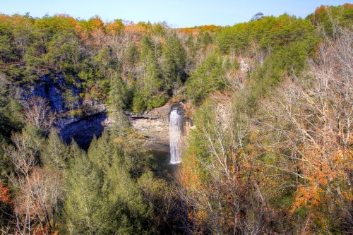 A scenic view of a waterfall surrounded by lush green trees and autumn foliage in a serene landscape.