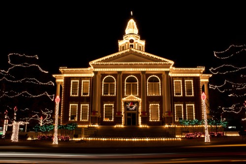 A beautifully lit historic building adorned with festive lights during the night, surrounded by holiday decorations.