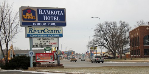 Signage for Ramkota Hotel and RiverCentre, with a view of a snowy street and various businesses in the background.