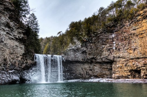 A serene waterfall cascades into a tranquil pool, surrounded by rocky cliffs and lush greenery.
