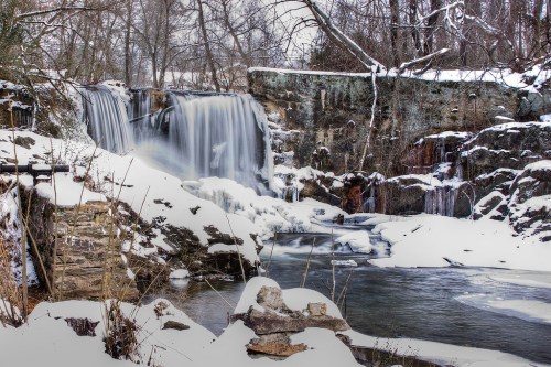 A serene winter scene featuring a waterfall surrounded by snow-covered rocks and icy water.