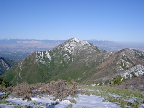 A scenic mountain view with snow-capped peaks and a clear blue sky, overlooking a valley below.