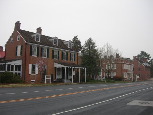 Two historic brick buildings line a quiet road, surrounded by trees and a foggy sky.