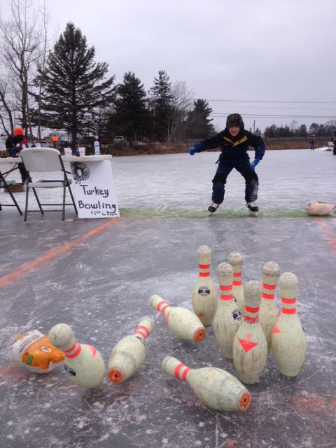 A person ice skating towards a set of bowling pins on a frozen surface, with a sign for "Turkey Bowling" nearby.