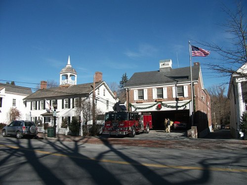 A quaint town scene featuring a fire truck, historic buildings, and an American flag under a clear blue sky.