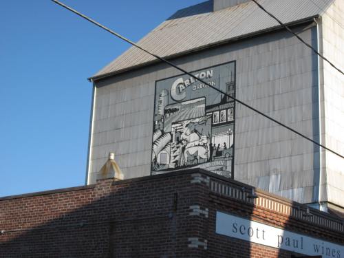 A mural on a building featuring vintage imagery, with a clear blue sky above and power lines in the foreground.