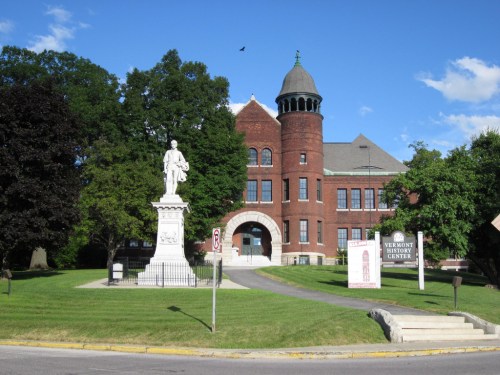 Historic brick building with a dome, surrounded by trees and a statue, featuring a sign for the Vermont History Center.