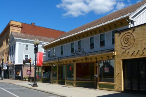 A street view of a small town with colorful storefronts and a blue sky with clouds.