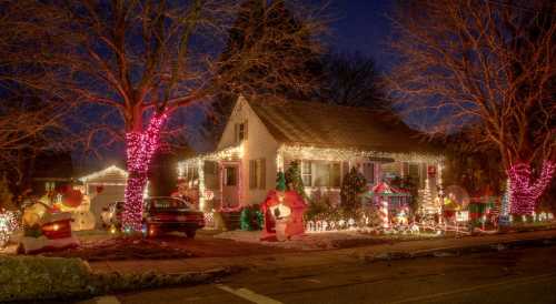 A festive house decorated with colorful Christmas lights, inflatable decorations, and a snowy yard at night.