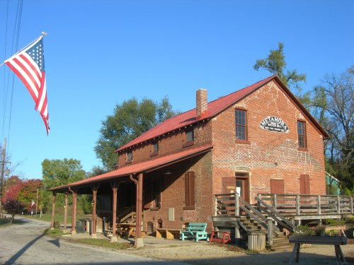 Historic brick building with a red roof, American flag flying, surrounded by trees and a clear blue sky.