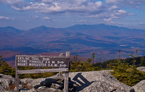 A wooden signpost points to Skyline Trail, Stowe Pinnacle, and Mount Worcester, with mountains and autumn foliage in the background.