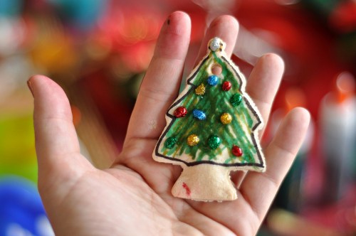 A hand holding a decorated Christmas tree ornament with colorful beads and green paint.