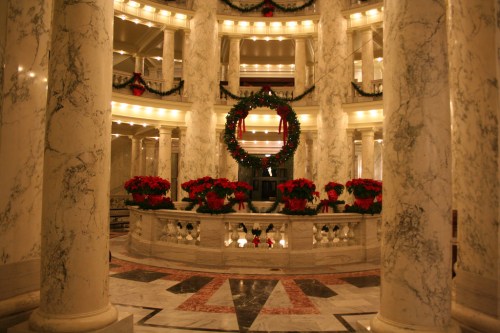 Elegant marble interior with festive wreaths and red poinsettias, illuminated by warm lights.