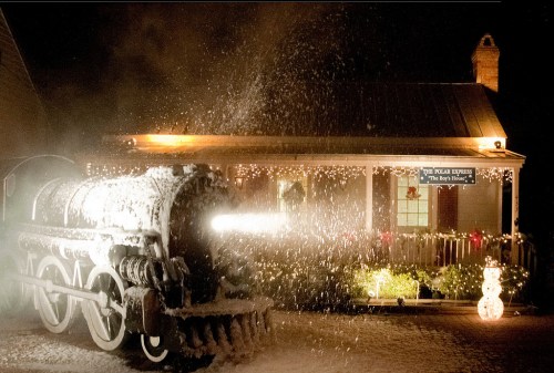 A snowy scene featuring a vintage train in front of a decorated house, illuminated with festive lights.