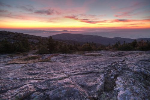 A scenic view of a rocky landscape at sunset, with vibrant colors in the sky and distant mountains.