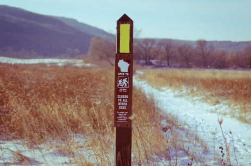 A trail marker in a snowy field, indicating open hiking trails and closed areas for other uses.