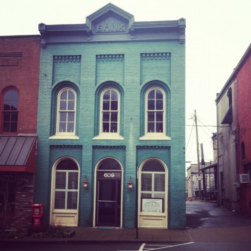 Historic teal bank building with large windows, located at 609, surrounded by other buildings on a quiet street.