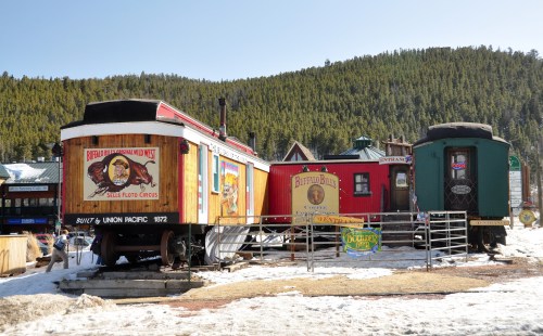 Colorful vintage train cars displayed in a snowy area, surrounded by trees and rustic signage.