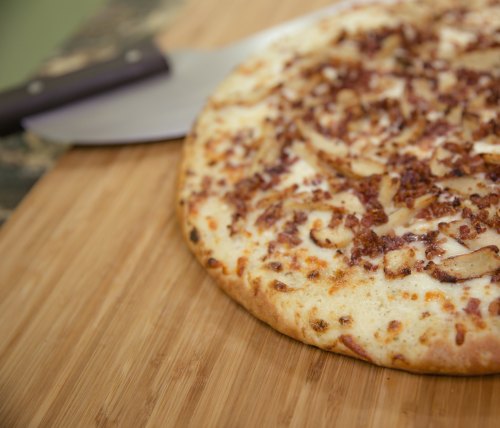 A freshly baked pizza topped with cheese and bacon, resting on a wooden cutting board with a pizza cutter nearby.