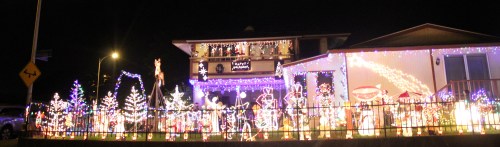 A house decorated with colorful Christmas lights and festive displays, glowing brightly at night.