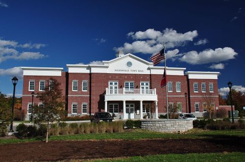 A brick building with a white portico, flags, and a blue sky, identified as the town hall of a small town.