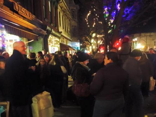 A bustling street scene at night, filled with people enjoying festive lights and decorations during a holiday event.
