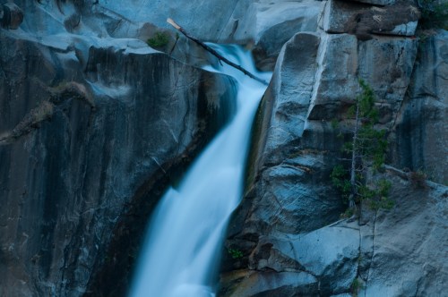 A serene waterfall cascading down rocky cliffs, surrounded by lush greenery and soft blue tones.