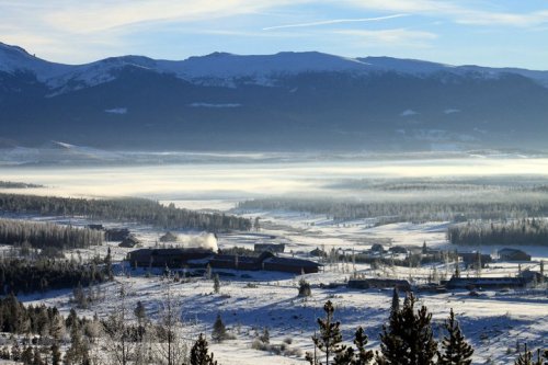 A snowy landscape with mountains in the background, featuring a valley shrouded in mist and a small industrial area.