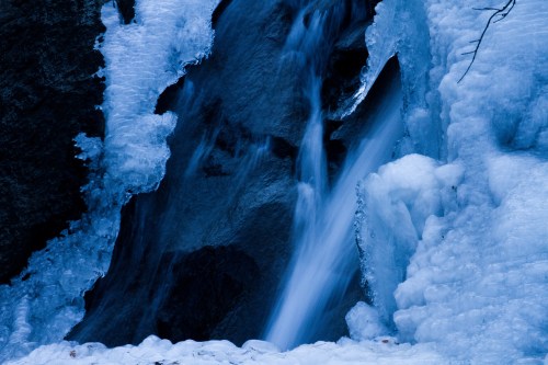 A serene waterfall surrounded by icy blue formations, creating a tranquil winter scene.
