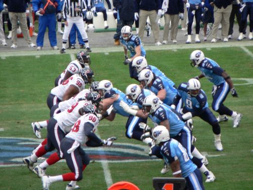 A football game scene with players from two teams lined up on the field, ready for the snap.