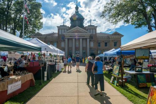 A bustling outdoor market with tents and vendors in front of a historic building under a blue sky.