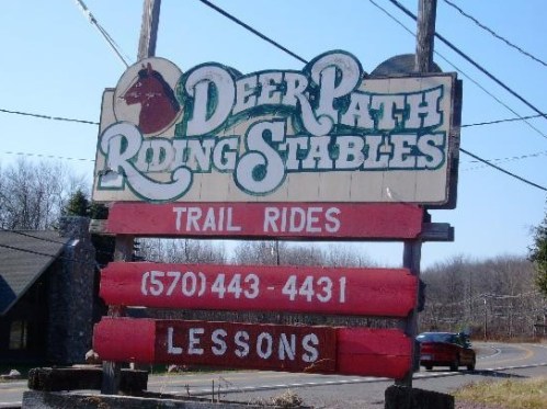 Sign for Deer Path Riding Stables, featuring trail rides and lessons, with a phone number for inquiries.