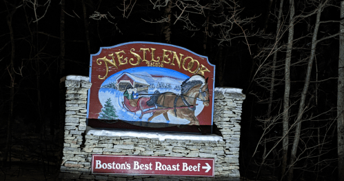A colorful sign for Nestlenook Estate, featuring a horse-drawn sleigh, surrounded by trees in a nighttime setting.