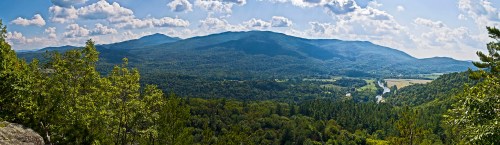 A panoramic view of lush green mountains under a bright blue sky with fluffy clouds.