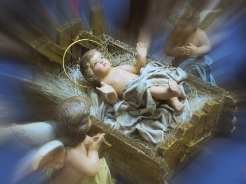 A serene nativity scene featuring a baby in a manger, surrounded by angels, with a soft, blurred background.