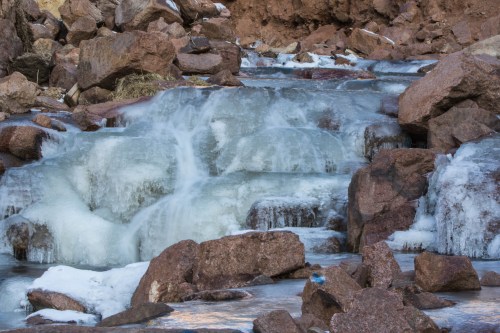 A frozen waterfall cascading over rocky terrain, surrounded by ice and snow.