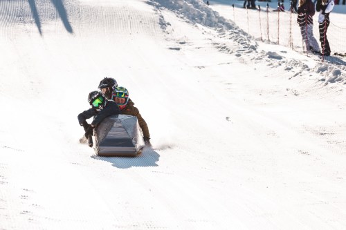 Three children sledding down a snowy hill, enjoying a sunny winter day.