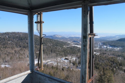 View from a lookout tower, showcasing a snowy landscape with mountains and valleys under a clear blue sky.