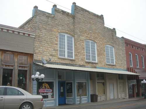 Historic stone building with large windows, featuring a storefront labeled "GAMEVAULT" and neighboring shops.