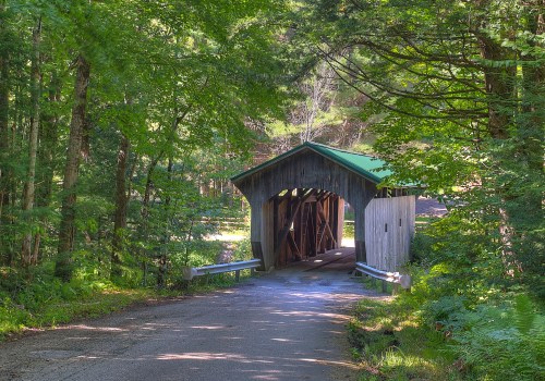 A rustic covered bridge surrounded by lush green trees, leading down a quiet, winding road.