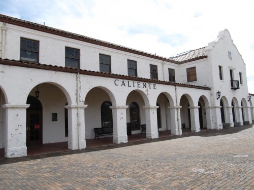 Historic building with arched entryways, white stucco walls, and a tiled roof, featuring the word "Caliente."
