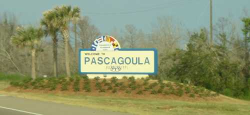 Welcome sign for Pascagoula, featuring colorful flags and greenery in the background.