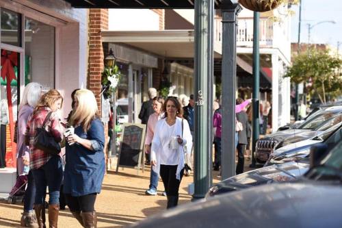 A busy street scene with people walking along shops, enjoying a sunny day in a small town.