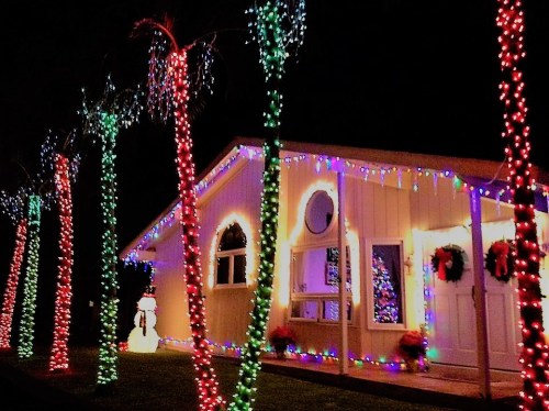 A brightly lit house decorated with colorful Christmas lights and a snowman in the yard at night.