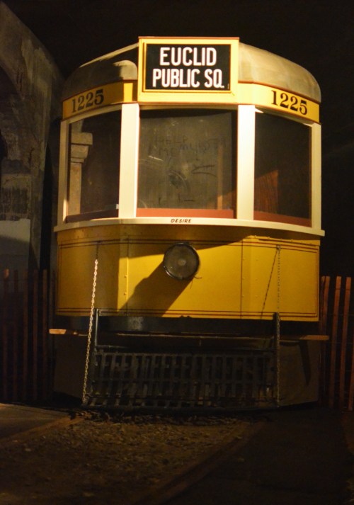 A vintage yellow streetcar with "Euclid Public Sq." sign, displayed in a dimly lit setting.