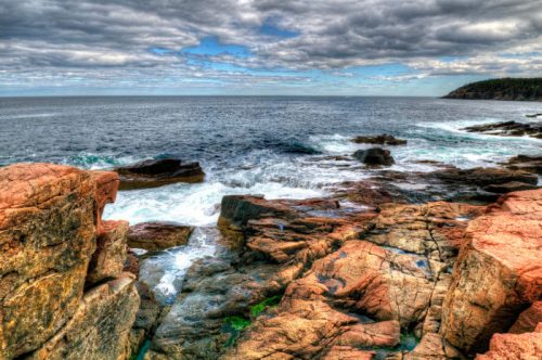 Rocky coastline with crashing waves under a cloudy sky, showcasing the beauty of the ocean and rugged terrain.