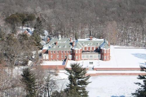 Aerial view of a large brick mansion surrounded by snow-covered trees and a white landscape.